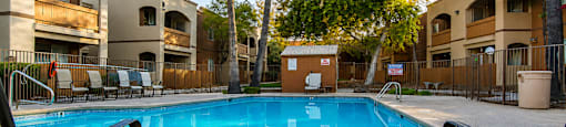 A pool surrounded by a fence and chairs with a building in the background.