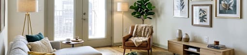 A living room with a grey couch, a wooden coffee table, a wooden cabinet, a ceiling fan, and a large window.