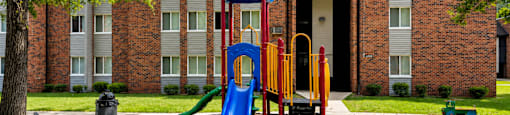 A playground with a blue slide and a yellow slide in front of a brick building.