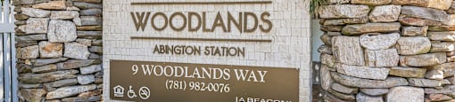 Property entrance sign with stone pillars at Woodlands at Abington Station Apartments, Abington, MA 2351