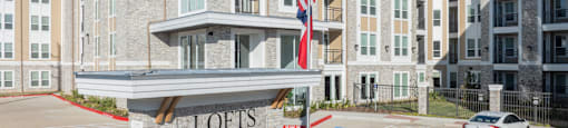 A large building with the name "Lofts at Katy Ranch" on a stone pillar in front.
