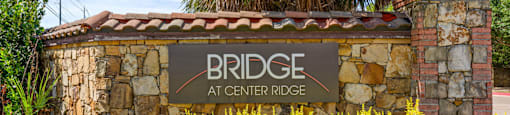 A sign that says "Bridge at Center Ridge" is in front of a palm tree.