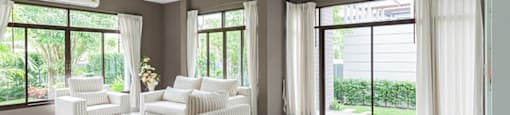 A spacious living room with a white sofa set and large windows.