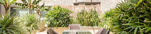 A patio with a table and chairs surrounded by green plants.
