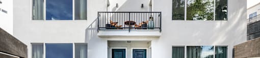 the front facade of a white house with blue doors and a balcony