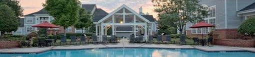 A swimming pool in front of a house with a sunset in the background.
