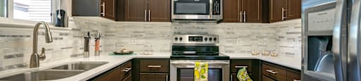 One-Bedroom Apartments in Walnut Creek, CA - Ivy Hill - Kitchen with Wood-Style Cabinetry, Stainless Steel Appliances, White Counters, and White/Grey Tile Backsplash