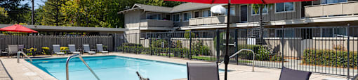 A red umbrella shades a table with chairs around a pool.