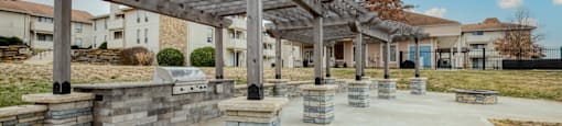 A concrete patio with a wooden pergola and stone pillars.