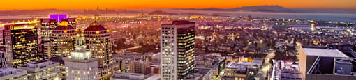 A cityscape at dusk with buildings illuminated against a twilight sky.