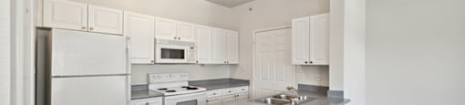 Apartments in North Dallas TX - Tivoli - Galley Kitchen with White Cabinetry, Grey Countertops, and All White Appliances