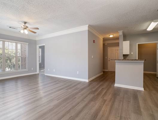 an empty living room with a kitchen in the background