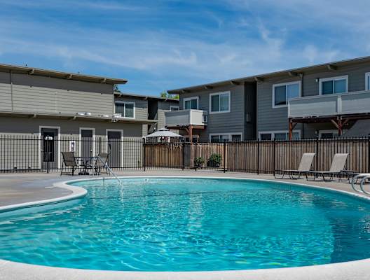 a swimming pool with chairs in front of an apartment building