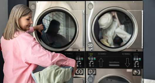 A woman in a pink shirt is loading a washing machine with clothes.
