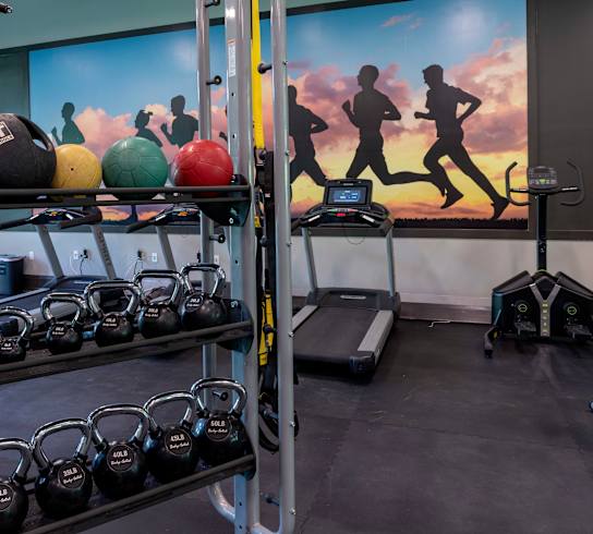 a gym with weights and a mural of runners on the wall