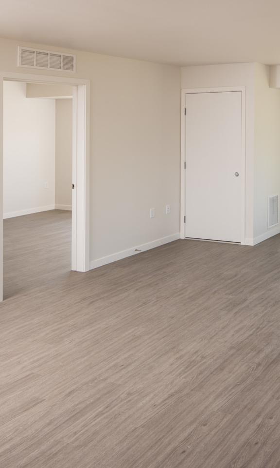A spacious room with light wood flooring and white walls.