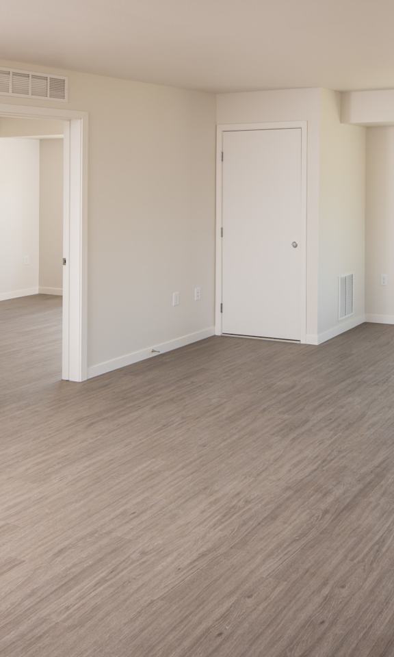 A spacious room with light wood flooring and white walls.