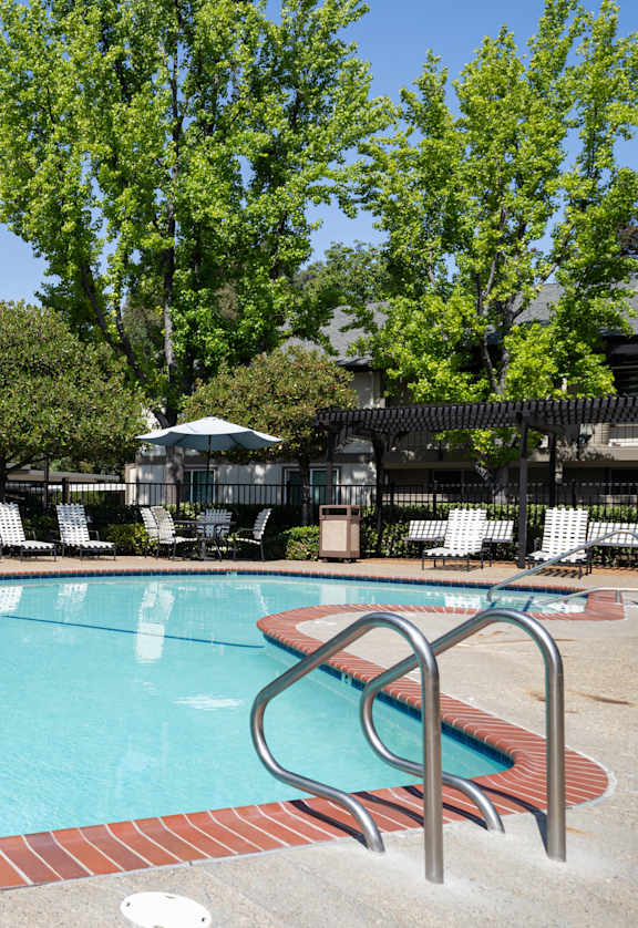 A swimming pool surrounded by trees and chairs.