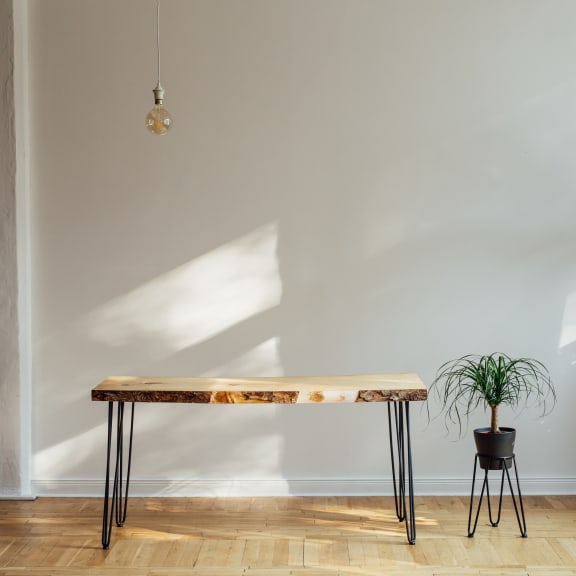 a wooden table with metal legs and a potted plant in front of a white wall