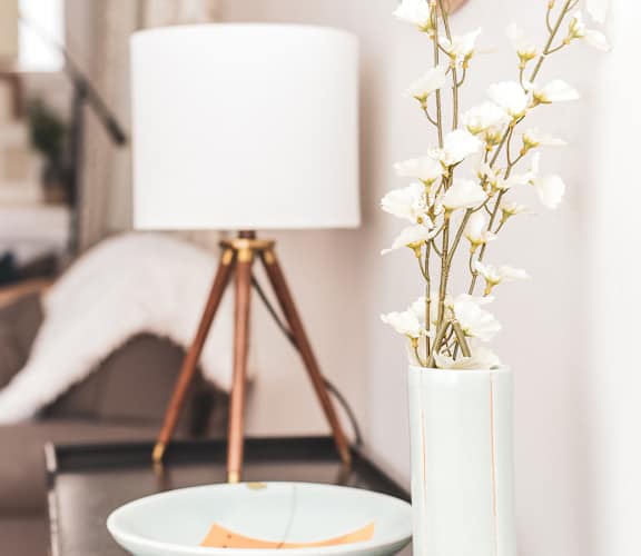 a living room with a lamp and a vase with white flowers