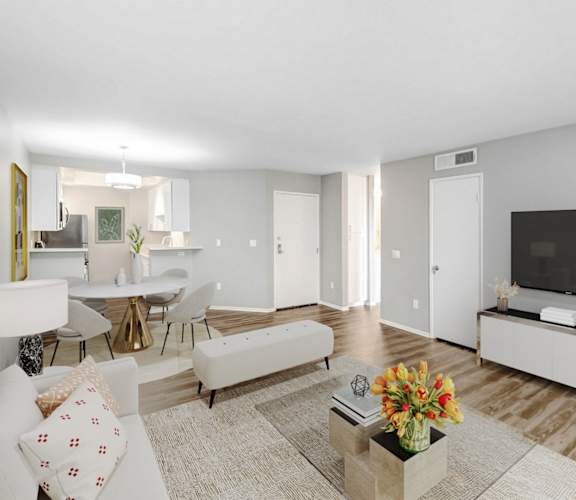 A living room with a white couch, a coffee table with flowers, and a television on a cabinet.