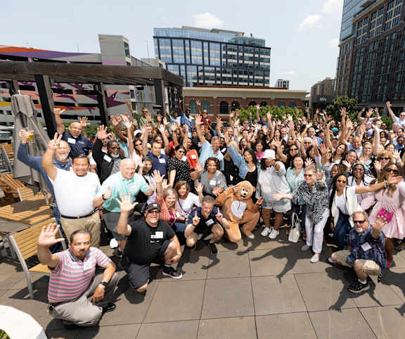 a large group of people posing for a photo with their hands up in the air