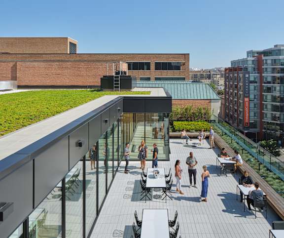 a roof deck with tables and chairs and a green roof on top of a building