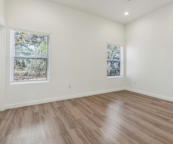 A room with wooden flooring and two windows.