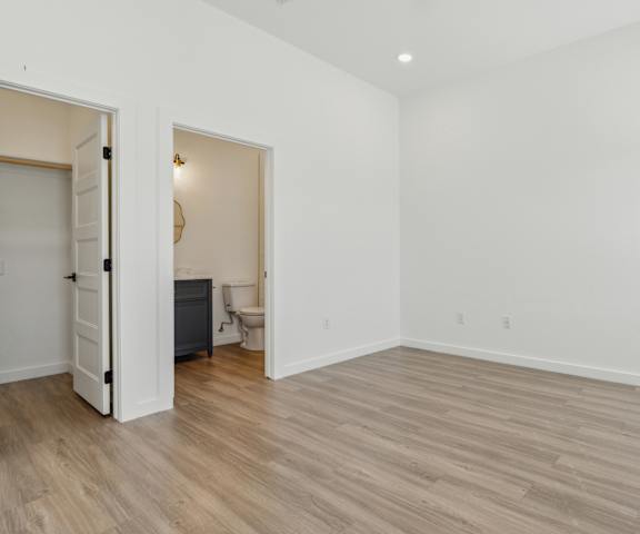 A room with a wooden floor and a doorway leading to a bathroom.