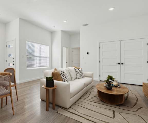 A modern living room with a white sofa, wooden coffee table, and a dining table with chairs.