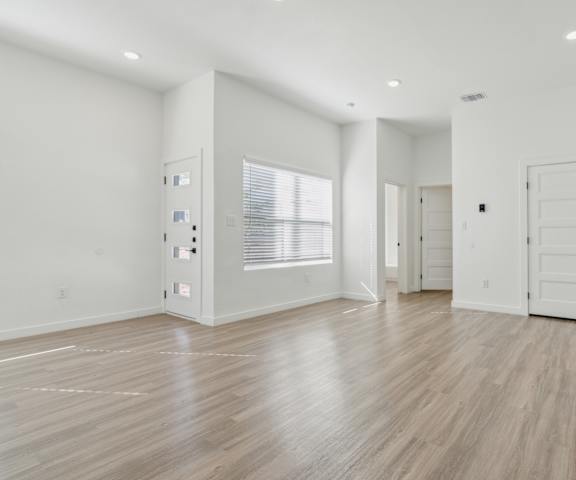 A spacious room with wooden flooring and white walls.