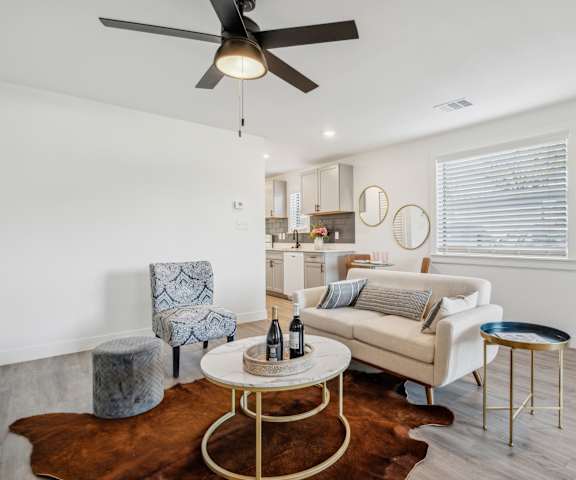 A living room with a white couch, a grey armchair, a round table with a bottle on it, and a brown cowhide rug.