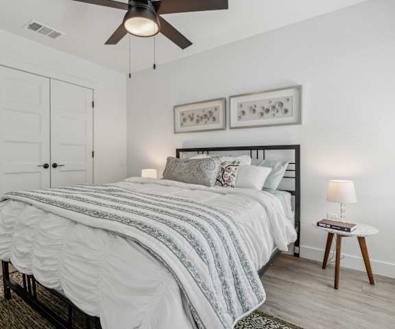 A bedroom with a bed, a ceiling fan, and a nightstand with a lamp.