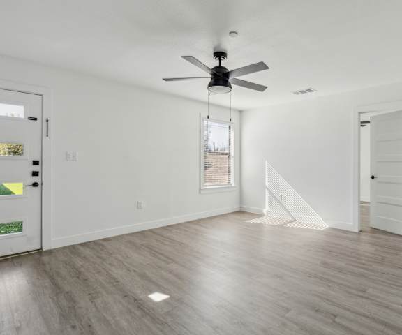 A room with a ceiling fan and light, hardwood floors, and white walls.