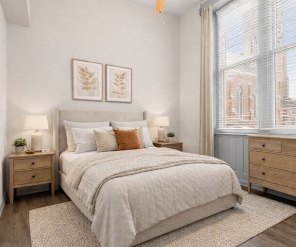 A bedroom with a large bed, two nightstands, and a window with a view of a cityscape.