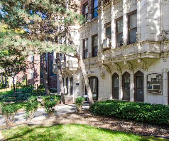 the facade of a building with a lawn and trees in front of it