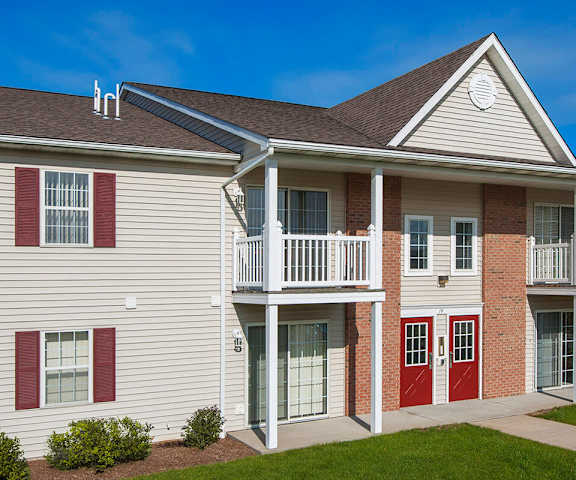 two-story apartment building with vinyl siding and brick accents, featuring shutters, patios, and balconies. The landscaping is neat, with modern design elements throughout