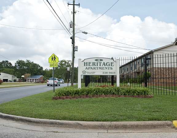 a sign that says heritage apartments in front of a black metal fence