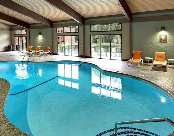 A large indoor swimming pool with a glass wall and orange lounge chairs.