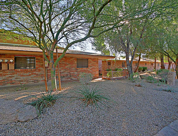the front yard of a brick house with a gravel driveway