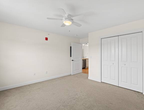 an empty living room with a ceiling fan and a closet