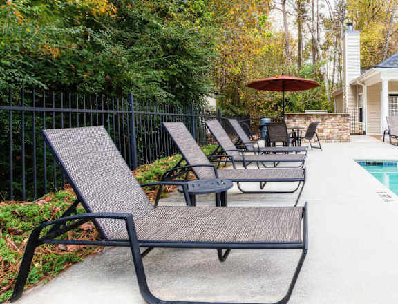 A poolside area with lounge chairs and a red umbrella.
