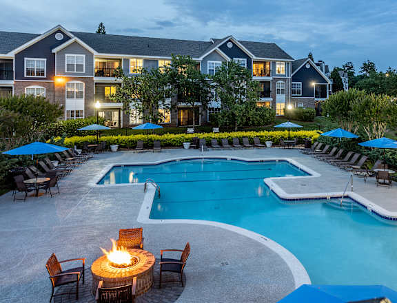 a swimming pool with a fire pit and patio furniture with an apartment building in the background