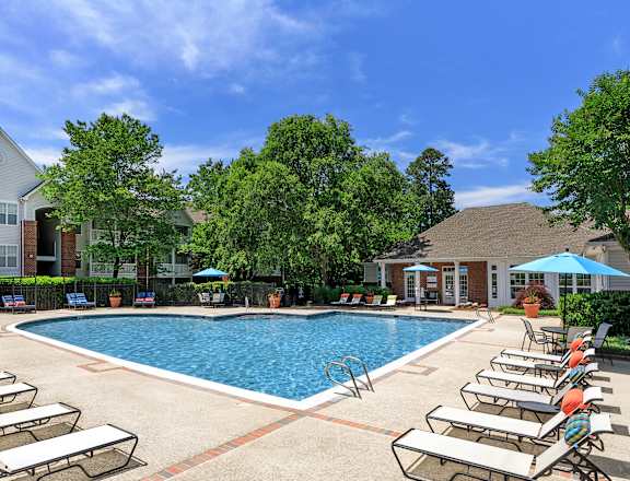 A pool surrounded by sun loungers and umbrellas with a building in the background.
