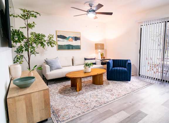 A living room with a white couch, a blue armchair, a wooden coffee table, and a flat-screen TV mounted on the wall.