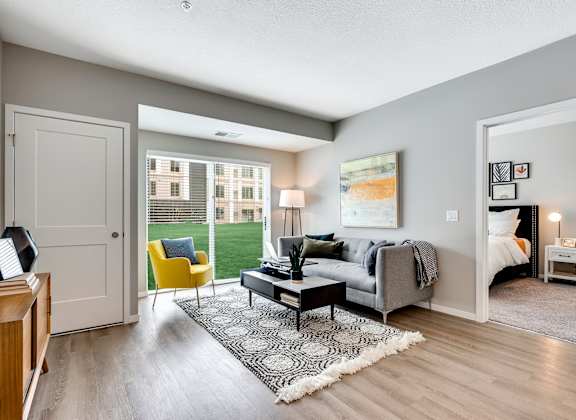 a living room with a gray couch and yellow chair and a sliding glass door leading to a