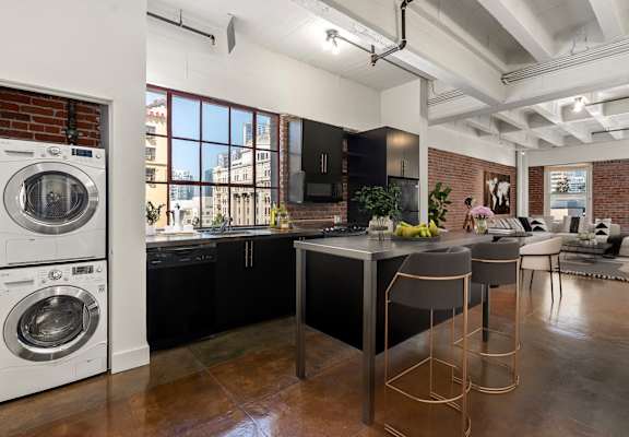 Kitchen with a washing machine and a kitchen island with chairs and a counter top at South Park Lofts, Los Angeles, California