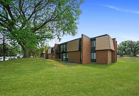 a row of brick apartments on a green lawn with a tree