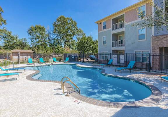 A swimming pool with a slide and sun loungers in front of a multi-story apartment building.