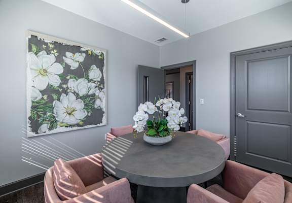 A grey table with a vase of flowers on it and two chairs with pink cushions.